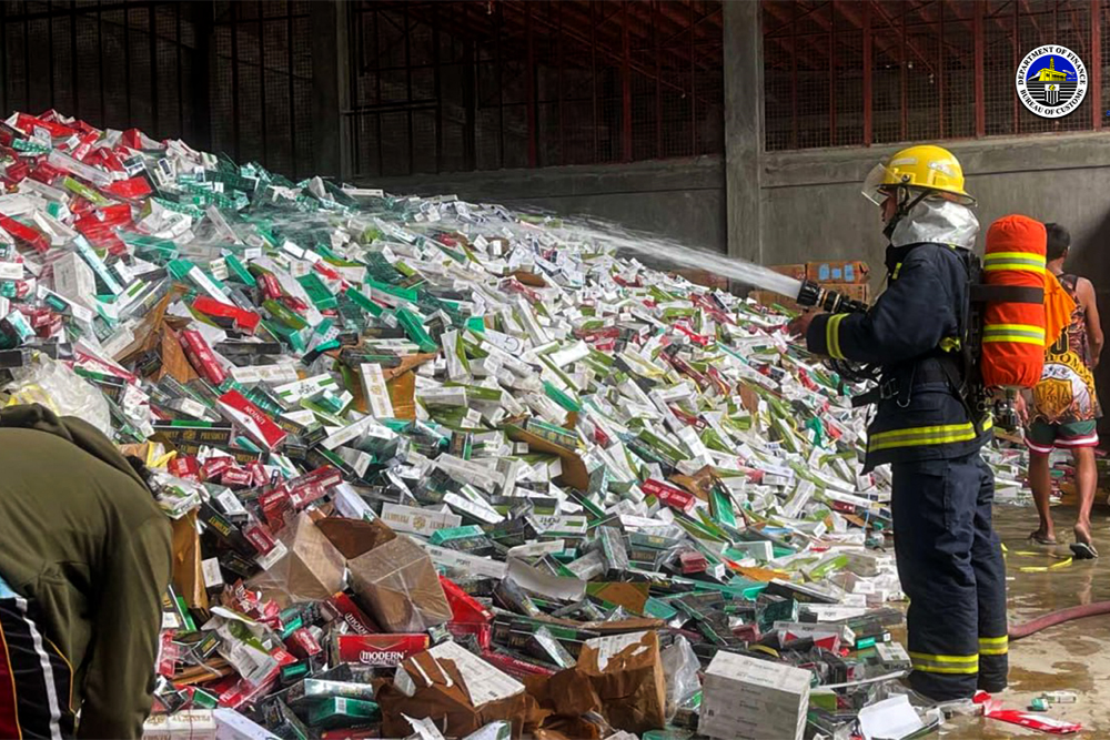 DESTROYED. A firefighter from the Bureau of Fire Protection (BFP) sprays water on contraband cigarettes worth PHP323 million at a warehouse rented by the Bureau of Customs (BOC) in Barangay Tetuan, Zamboanga City on Thursday (Nov. 30, 2023). The cigarettes, which were seized from May to November this year, were subsequently crushed by payloader equipment and then disposed of in the sanitary landfill in Barangay Salaan, Zamboanga City. (Photo courtesy of BOC-Port of Zamboanga)